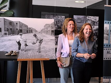 Kleurenfoto van twee vrouwen met zwart wit foto op achtergrond waar ze 44 jaar geleden werden gefotofafeerd