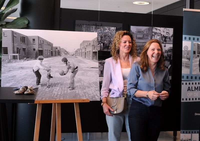 Kleurenfoto van twee vrouwen met zwart wit foto op achtergrond waar ze 44 jaar geleden werden gefotofafeerd
