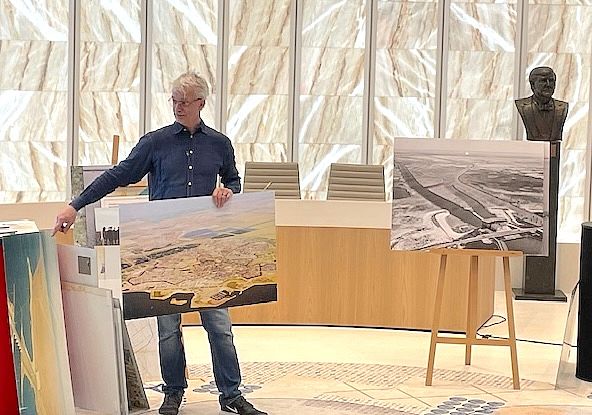 Michel Langendijk staat met een grote luchtfoto van Almere (in kleur) in zijn hand. Rechts van hem staat een andere luchtfoto in zwart-wit.