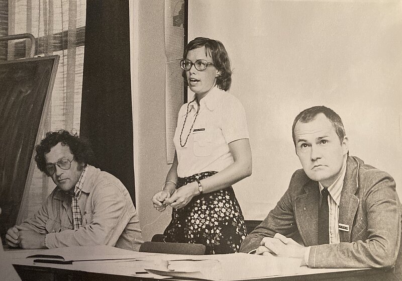 Zwart wit foto van Hanni Holtkamp, de eerste voorlichter van Almere tijdens een voorlichtingsbijeenkomst in De Kern, 17 juni 1974, rechts op de foto Dirk Frieling, directeur Projektburo Almere en links projectleider Hans Laumanns
