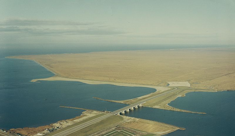 Luchtfoto Almere, Hollandsebrug (oriëntatie noord) Werkzaamheden bij de in 1969 open gestelde Hollandsebrug. Rijksweg 6 eindigt nog net in Flevoland in een rotonde met aansluitingen op de Gooimeerdijk (rechts) en de IJmeerdijk. De polder zelf is nog geheel agrarisch ingericht met gewassen die water onttrekken aan de bodem. Vaag zichtbaar in de verte gemaal de Blocq van Kuffeler.